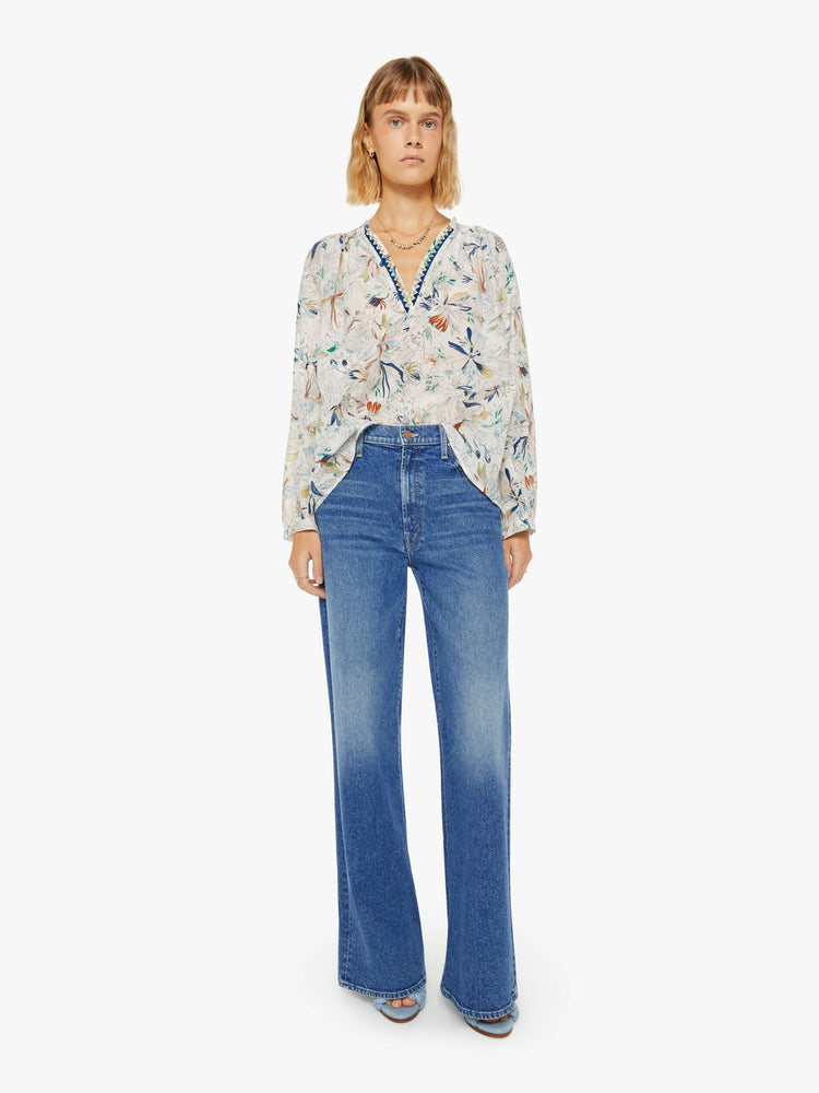 Full body view of a woman blouse with a deep V-neck, long sleeves and flowy fit in off white with colorful floral print and blue trim.