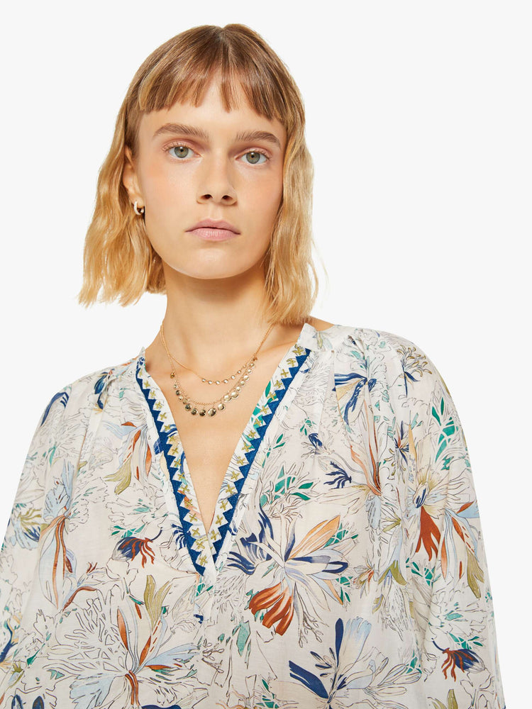 Close up view of a woman blouse with a deep V-neck, long sleeves and flowy fit in off white with colorful floral print and blue trim.