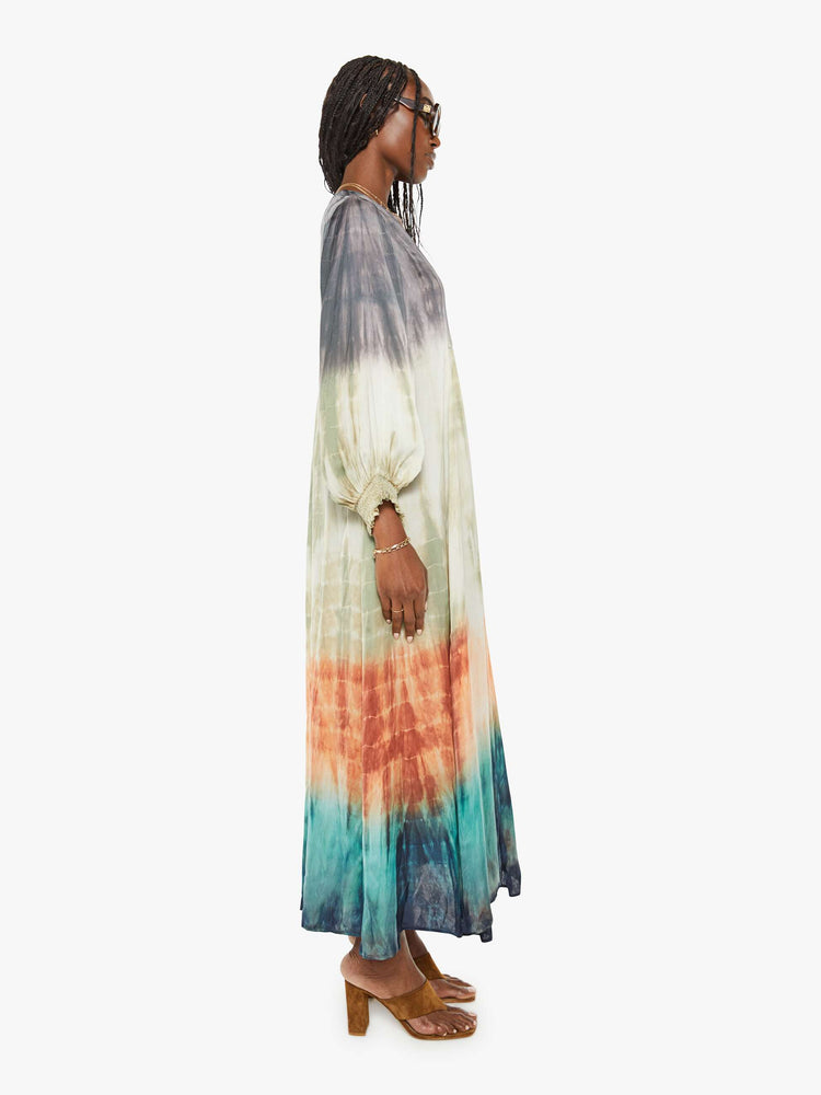 Side view of a woman maxi dress with a V-neck, cropped balloon sleeves and a loose, flowy fit in grey, green, orange, and blue ombre.