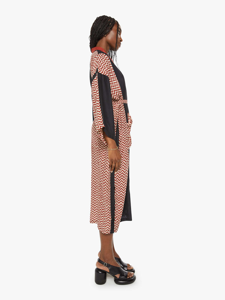 Side view of a woman robe with colorblocked silk in black and a red-and-white zig zag print, and features drop shoulders, a calf-length hem and a loose, flowy fit.