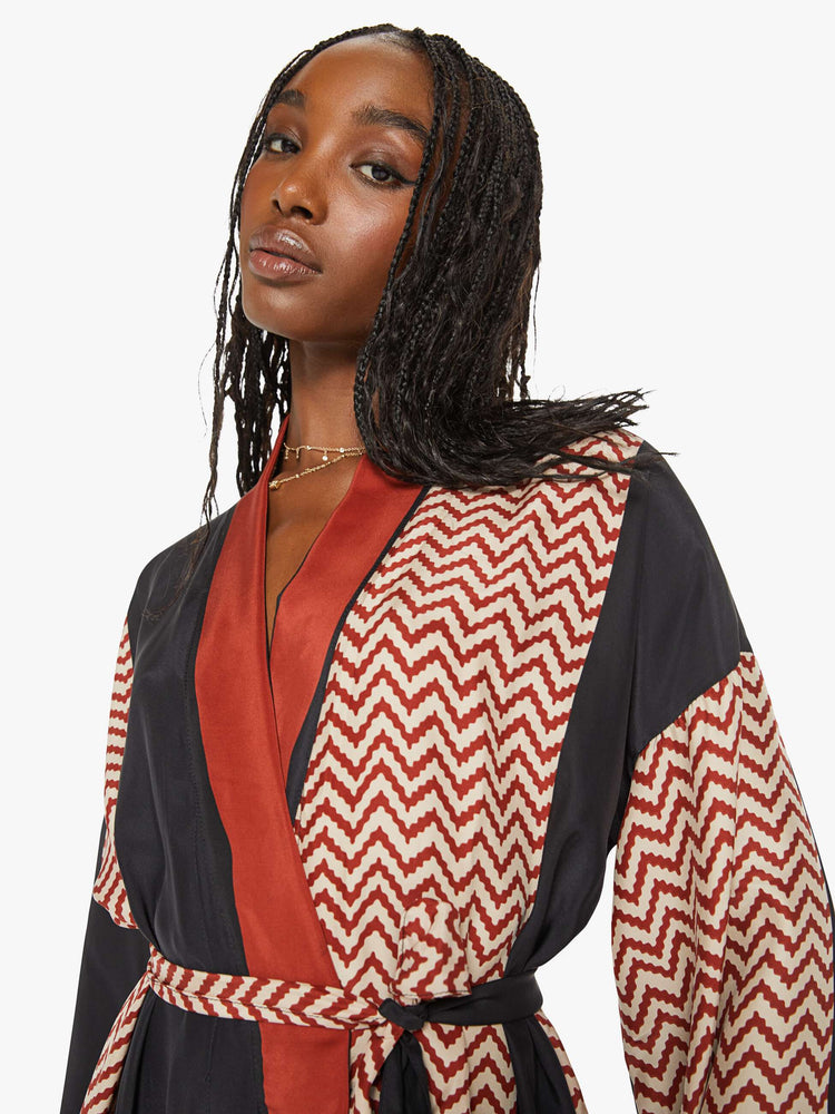 Close up view of a woman robe with colorblocked silk in black and a red-and-white zig zag print, and features drop shoulders, a calf-length hem and a loose, flowy fit.