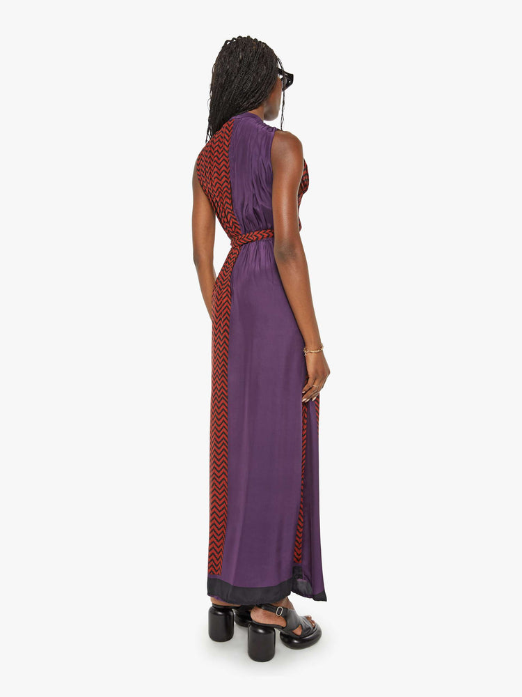 Back view of a woman purple and red zig zag print with a maxi dress V-with a neck, fitted waist that ties and ankle-length hem.