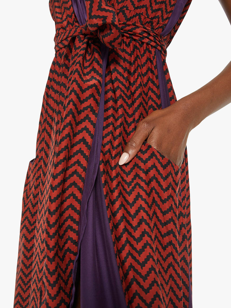 Close detail view of a woman purple and red zig zag print with a maxi dress V-with a neck, fitted waist that ties and ankle-length hem.