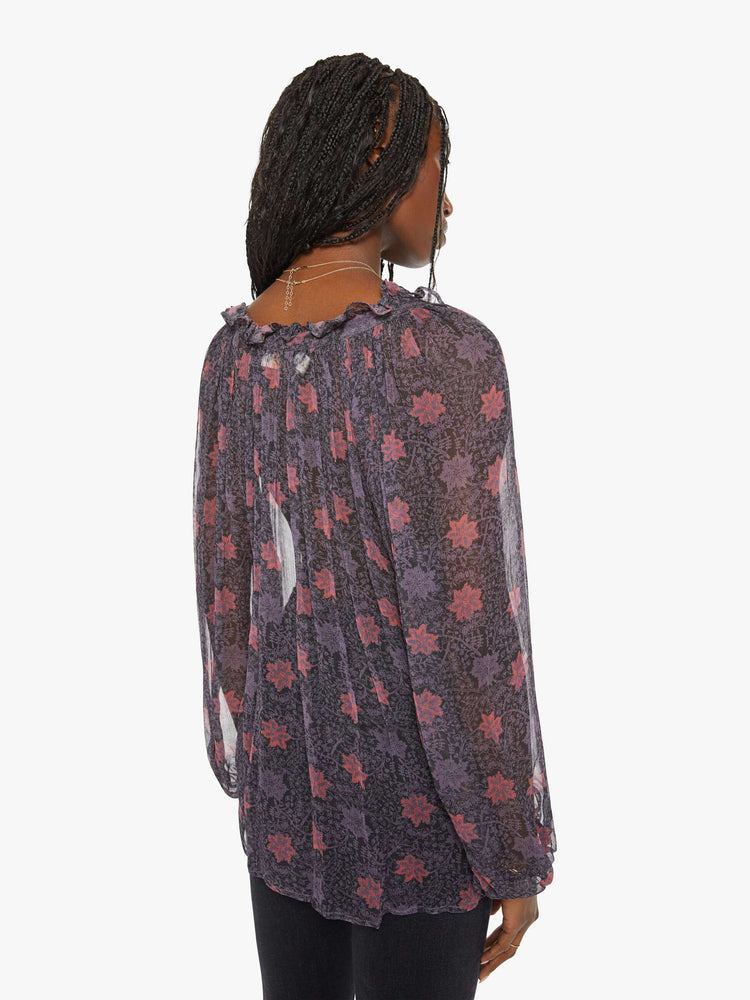 Back view of a woman top in a sheer purple fabric with red floral print and a top has a keyhole neckline with a tasseled tie closure, long balloon sleeves and pleats for a loose fit.