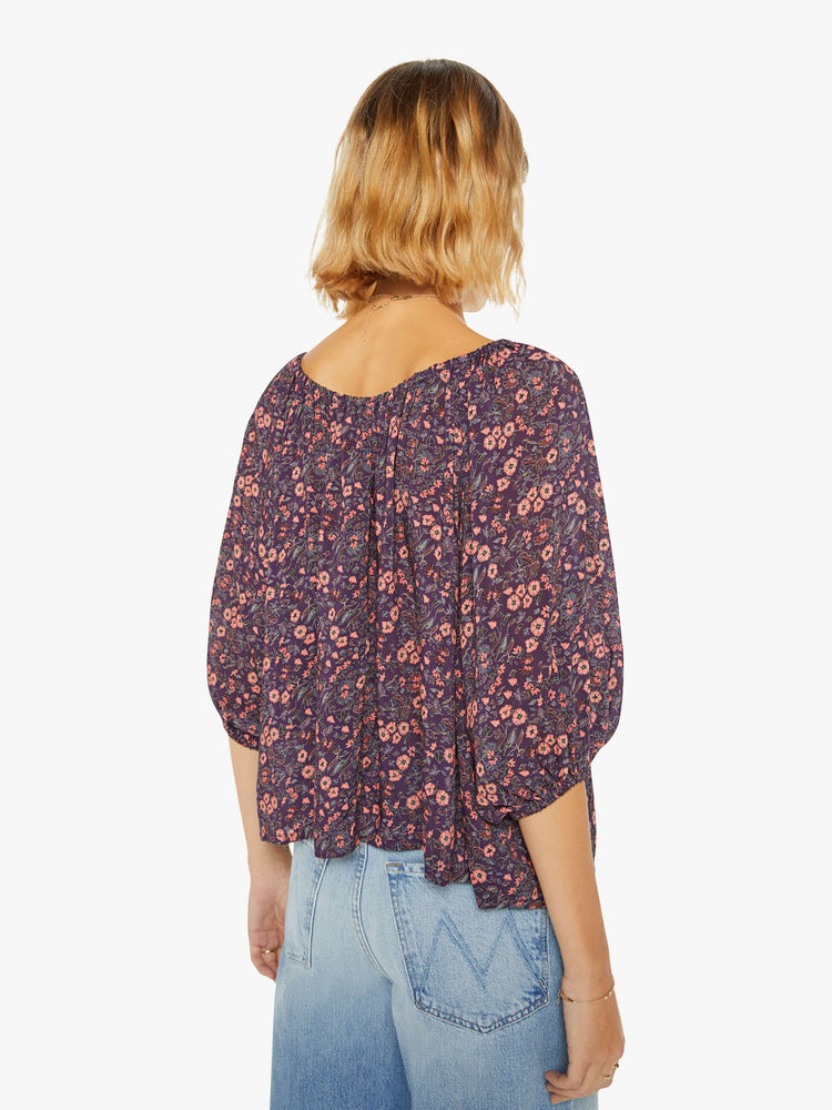 Back view of a woman blouse in a purple and pink floral print and features an elastic boat neck that can be worn off-the-shoulder, 3/4-length balloon sleeves and a flowy fit.