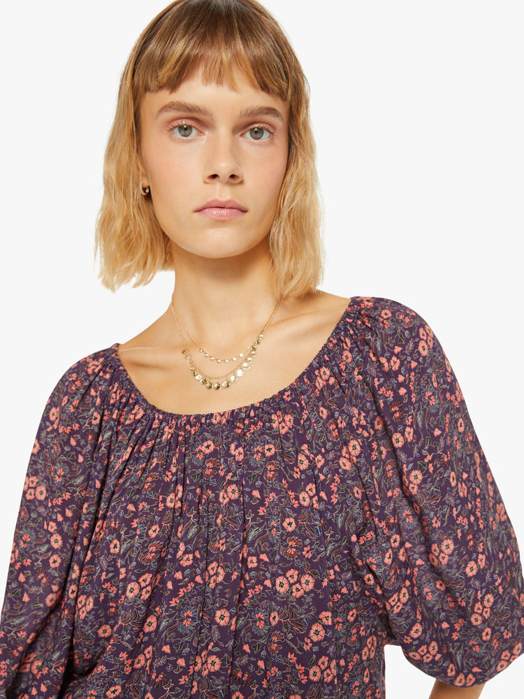 Close up view of a woman blouse in a purple and pink floral print and features an elastic boat neck that can be worn off-the-shoulder, 3/4-length balloon sleeves and a flowy fit.