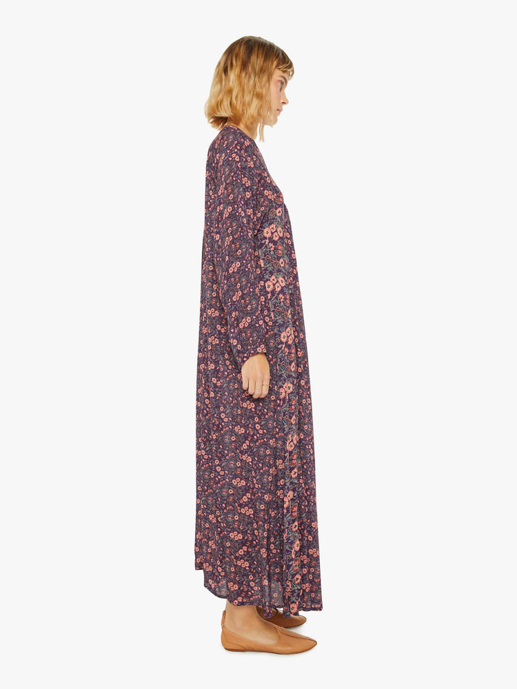 Side view of a woman purple and pink floral print maxi dress with voluminous sleeves and has an A-line cut for a loose, breezy feel.