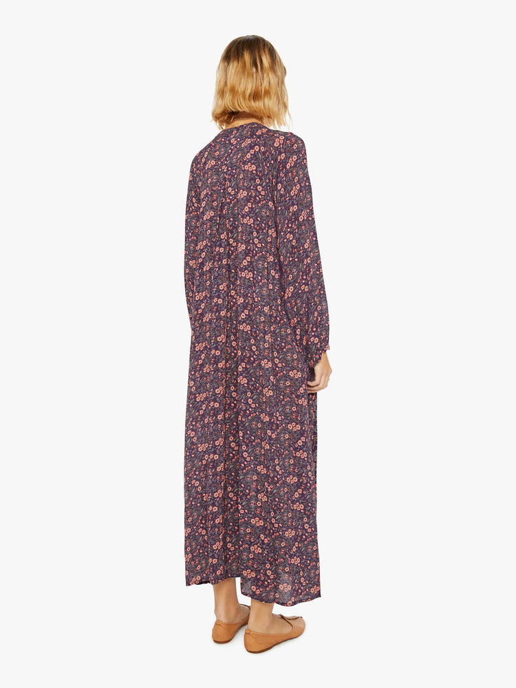 Back view of a woman purple and pink floral print maxi dress with voluminous sleeves and has an A-line cut for a loose, breezy feel.