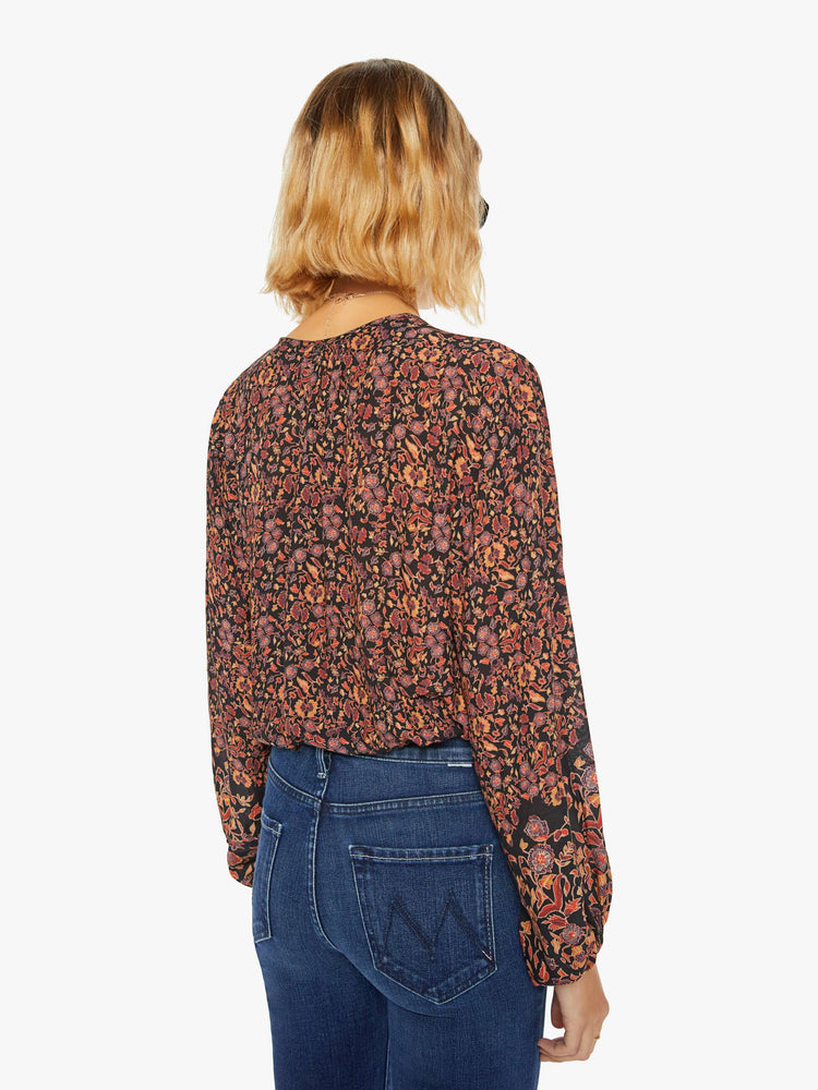 Back view of a woman top in black toned floral print with a keyhole neckline with a tasseled tie closure, drop shoulders, long balloon sleeves and a cropped elastic hem.