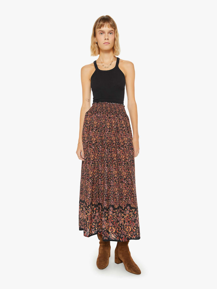 Front view of a woman maxi skirt in a warm toned floral print with a smocked waistband and a loose, flowy fit.