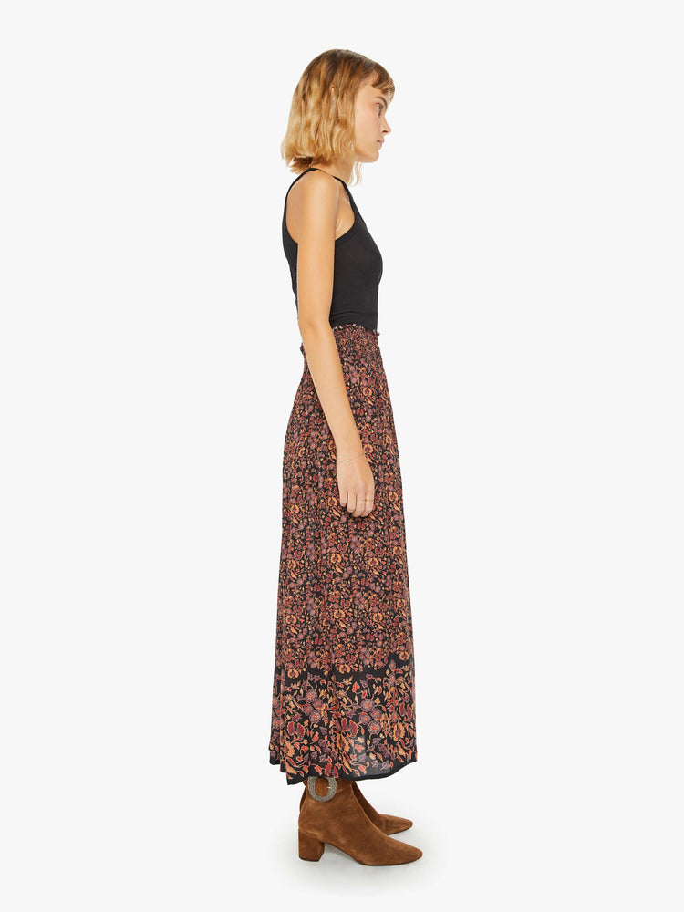 Side view of a woman maxi skirt in a warm toned floral print with a smocked waistband and a loose, flowy fit.