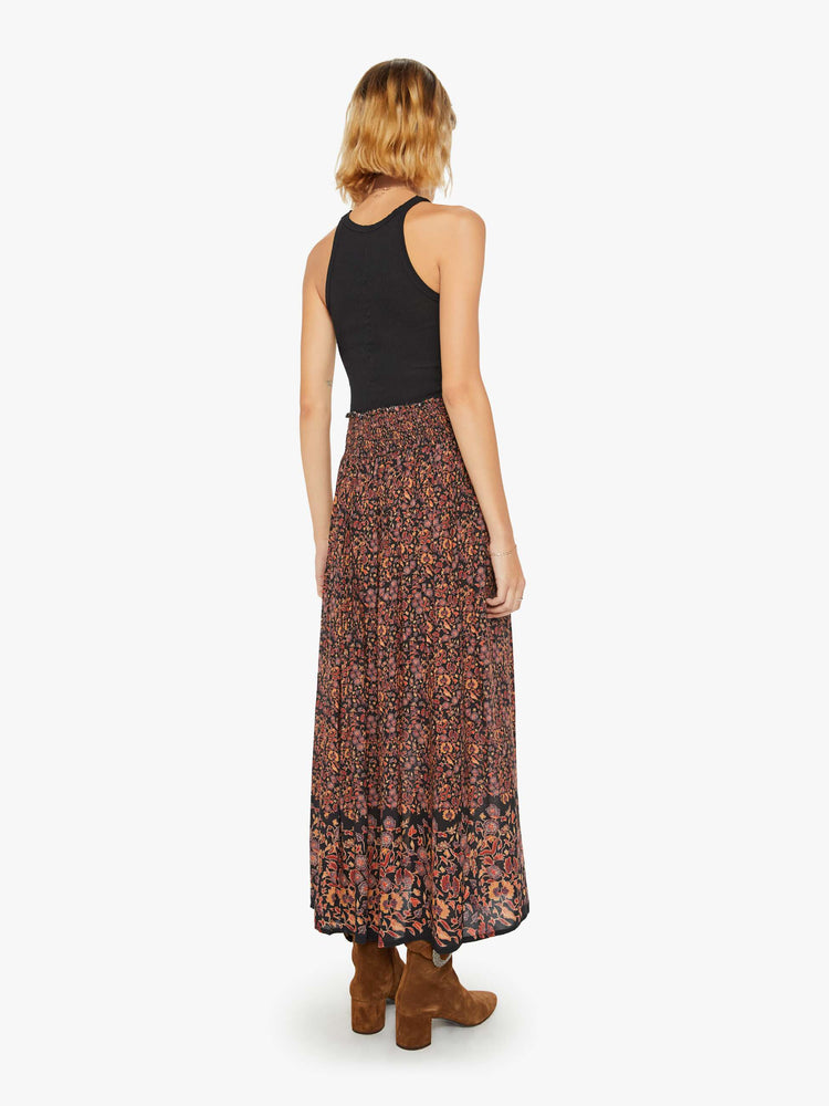 Back view of a woman maxi skirt in a warm toned floral print with a smocked waistband and a loose, flowy fit.