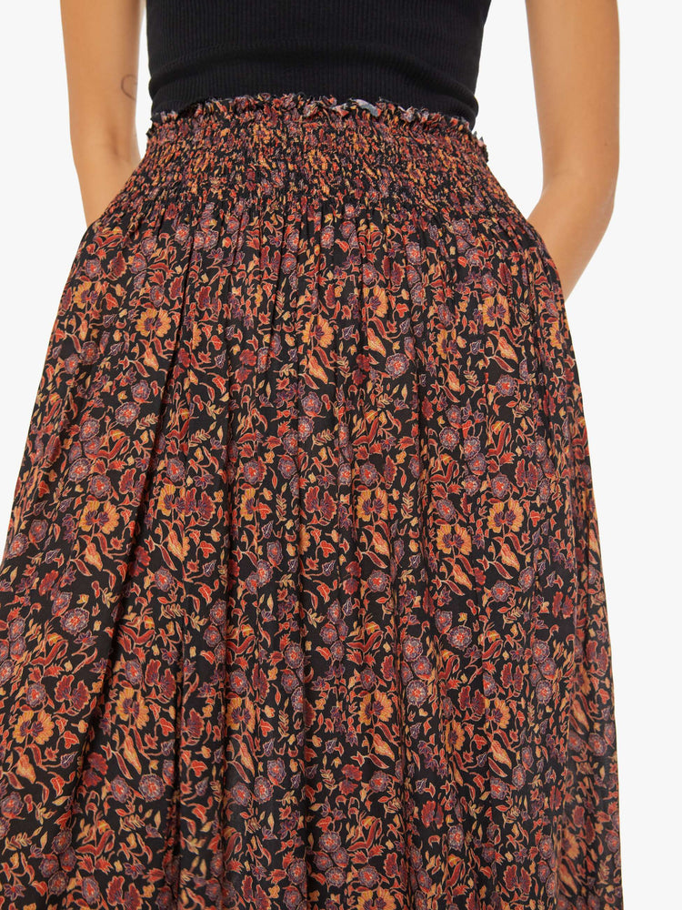 Close up waist view of a woman maxi skirt in a warm toned floral print with a smocked waistband and a loose, flowy fit.