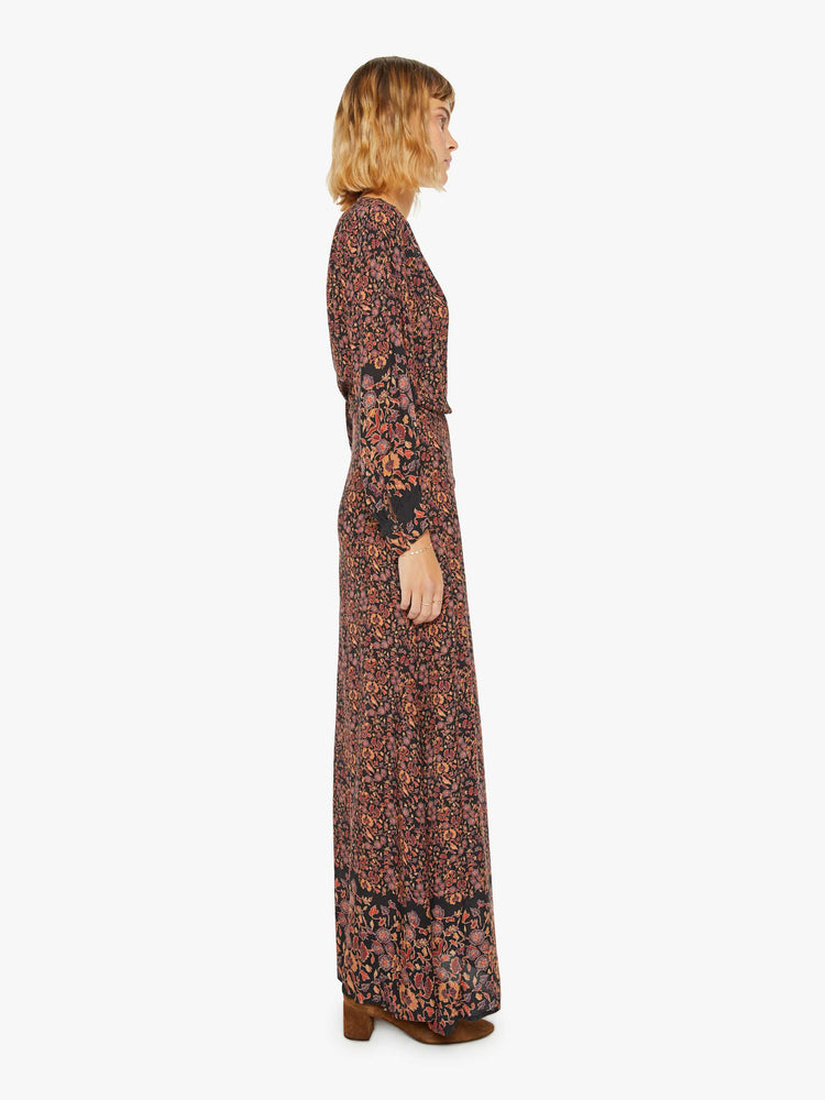 Side view of woman long sleeve dress in a warm tone floral print, and features a V-neck, tied waist and long maxi skirt with a loose, flowy fit.