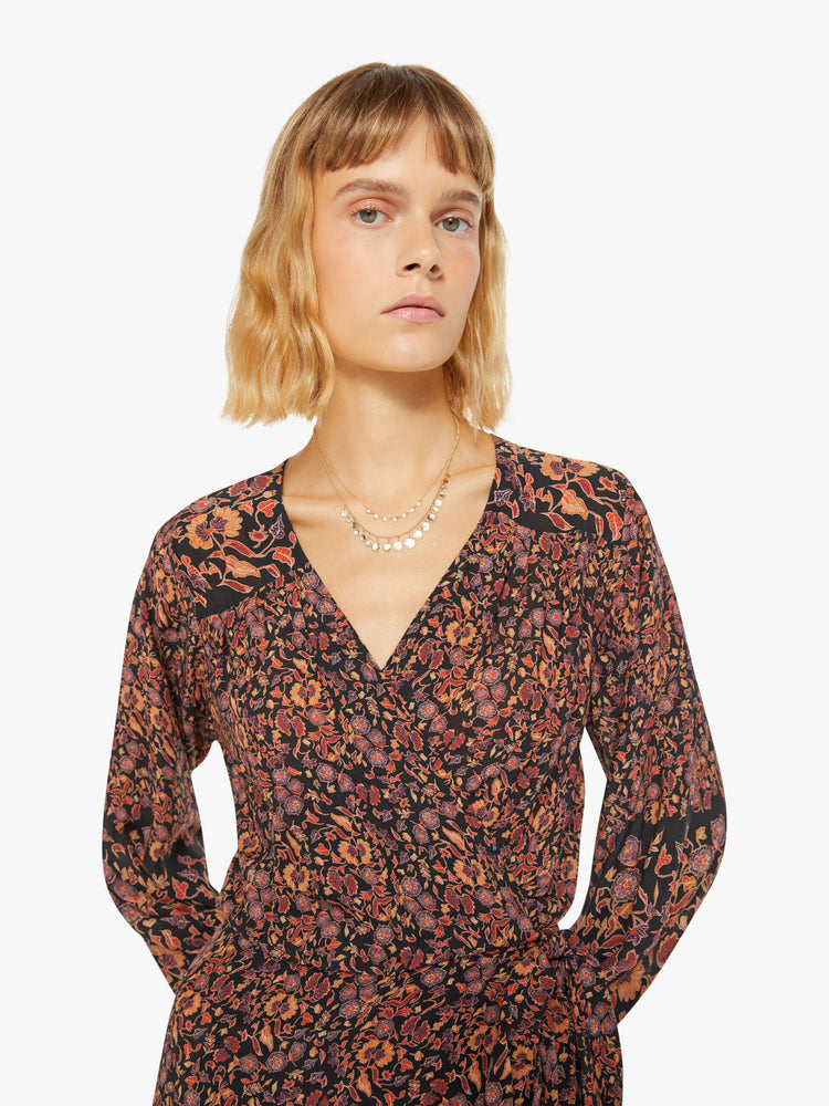 Close up view of woman long sleeve dress in a warm tone floral print, and features a V-neck, tied waist and long maxi skirt with a loose, flowy fit.