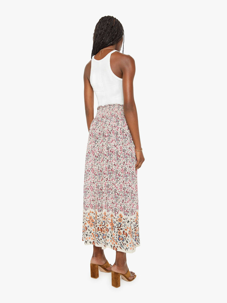 Back view of a woman in a white with a cool-toned floral print, and features a smocked waistband and a loose, flowy fit skirt.