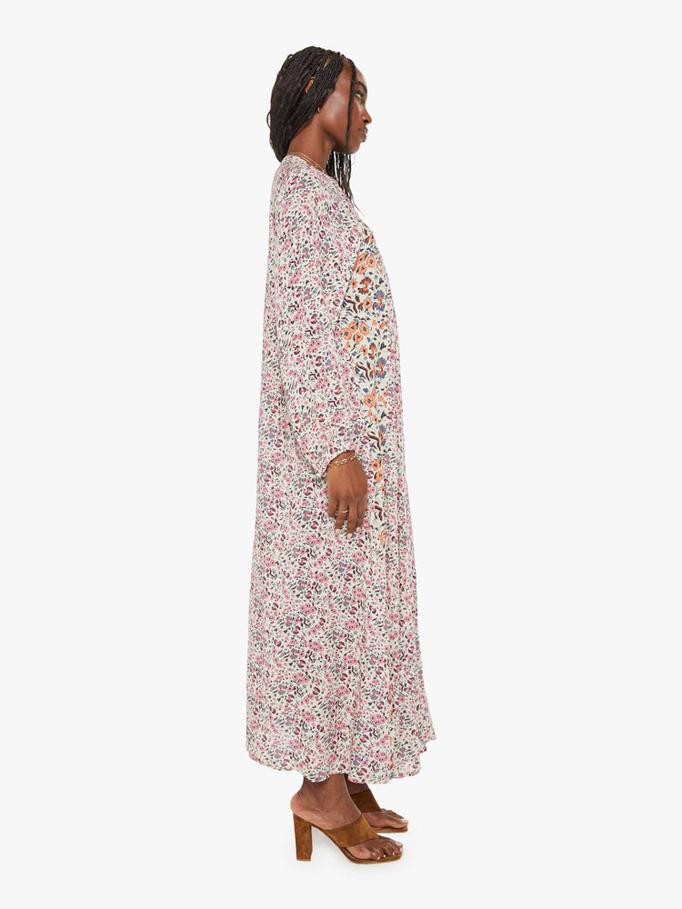 Side view of a woman in white with a multi-color floral print, this maxi dress is designed with voluminous sleeves and has an A-line cut for a loose, breezy feel.