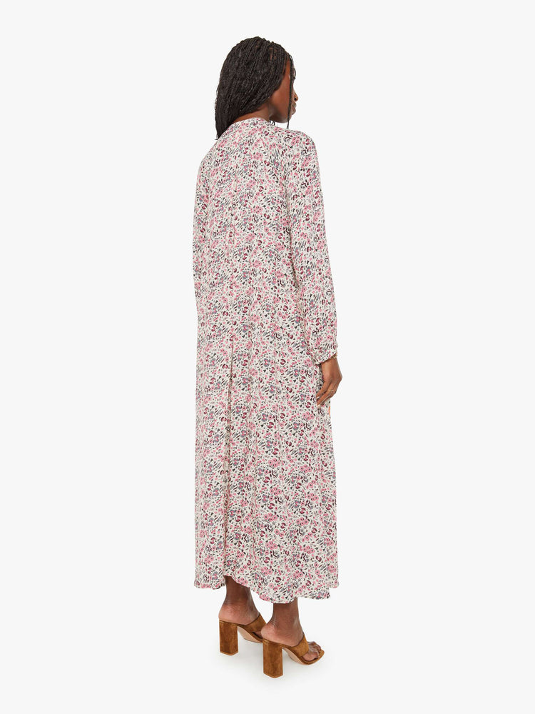 Back view of a woman in white with a multi-color floral print, this maxi dress is designed with voluminous sleeves and has an A-line cut for a loose, breezy feel.