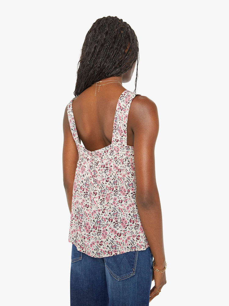 Back view of a woman in white with a multi-color floral print, and features detailed straps and buttons in the back top.