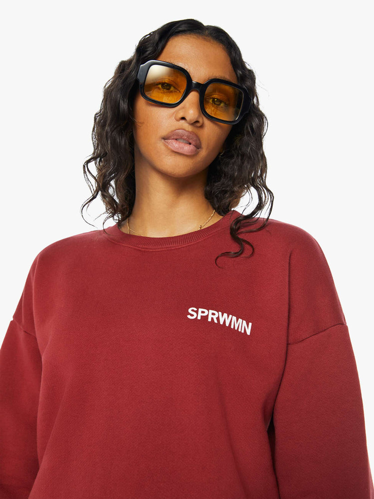 Close up view of a woman crewneck sweatshirt with the brands logo on the front in crimson red hue.