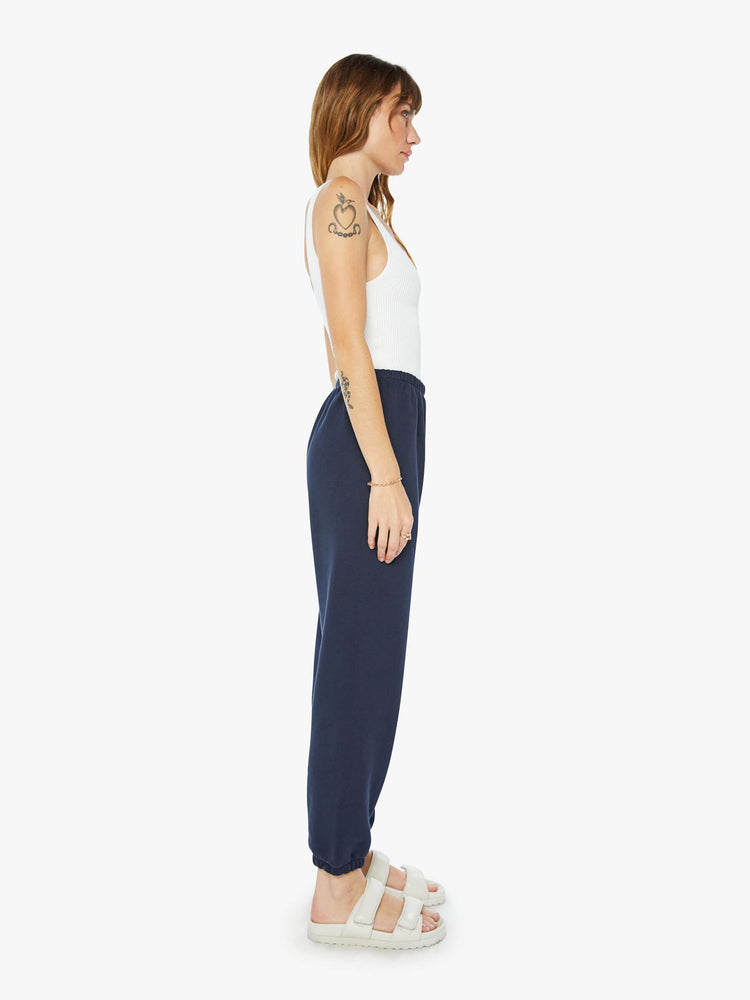 Side view of a woman navy with a white heart on the hip sweatpants with an elastic waist and cuffs for a loose, comfortable fit.