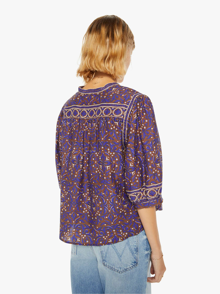 Back view of a woman in a maroon, purple and cream print with a V-neck, elbow-length balloon sleeves and a loose fit.