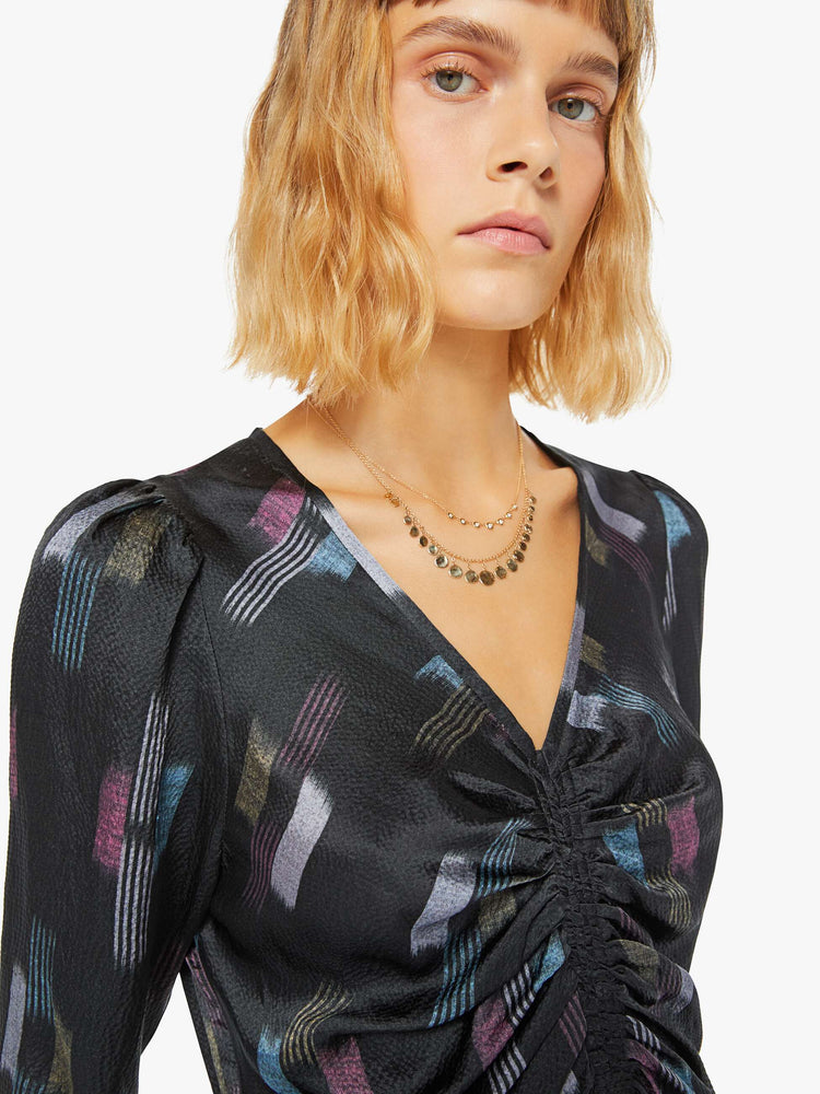 Close up view of a womans black dress with cool toned graphic print with deep V-neck, gathered bodice, long sleeves and a calf-length hem.