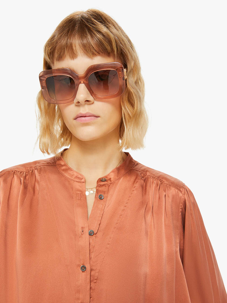 Close up view of a woman buttoned V-neck, long balloon sleeves and a flowy fit long sleeve in a burnt orange hue.
