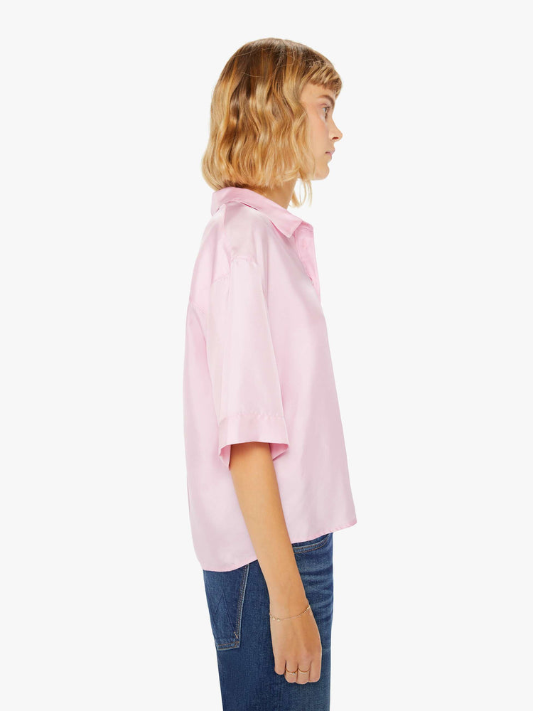 Side view of a woman pink short sleeve button-down with a collared neck, drop shoulders, oversized short sleeves and a boxy fit.