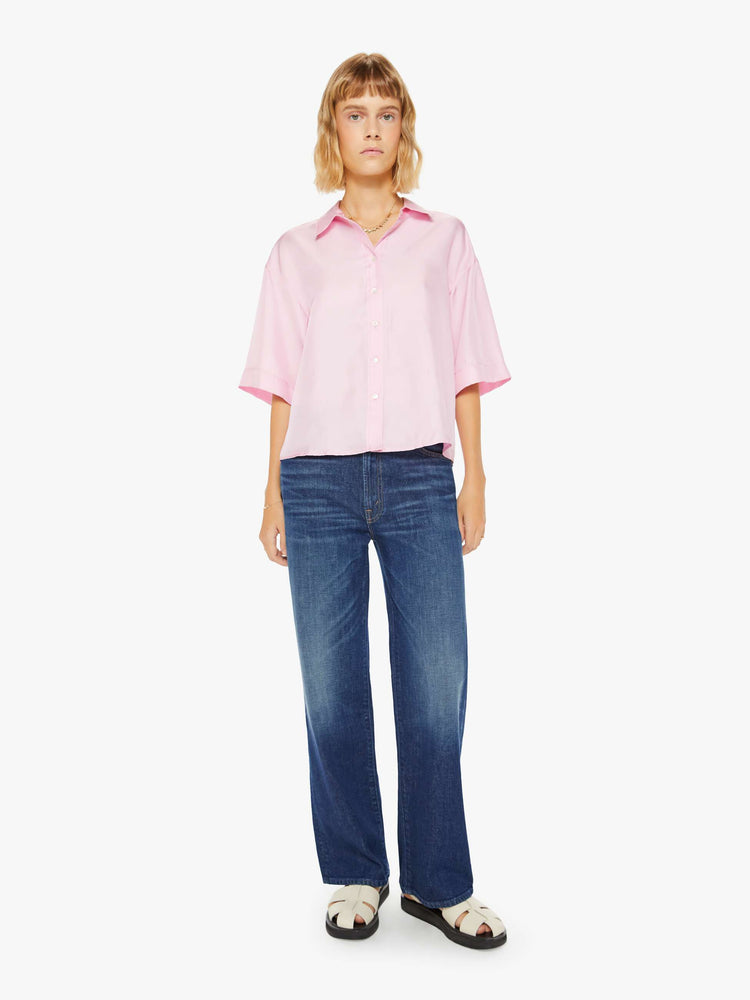 Full body view of a woman pink short sleeve button-down with a collared neck, drop shoulders, oversized short sleeves and a boxy fit.