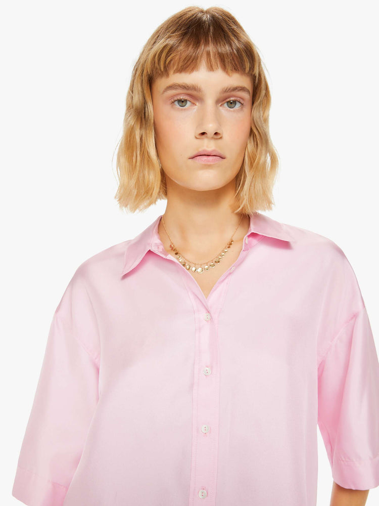 Close up view of a woman pink short sleeve button-down with a collared neck, drop shoulders, oversized short sleeves and a boxy fit.