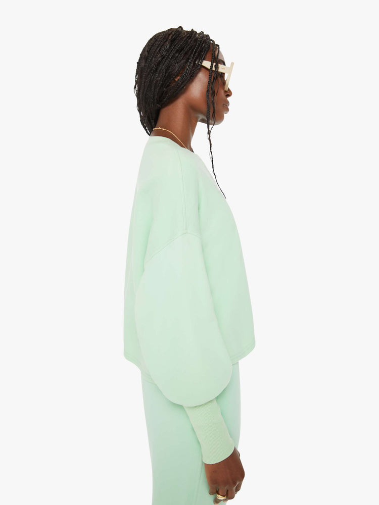 Side view of a woman minty- green hue crewneck sweatshirt with drop shoulders, bat-wing sleeves, extra-long ribbed hems at the wrists and a cropped, oversized fit.