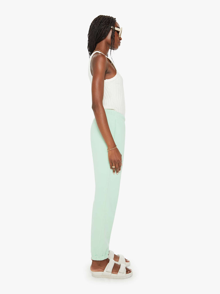 Side view of a woman mint green sweatpants with an elastic waist and hems, a high rise and a loose fit.