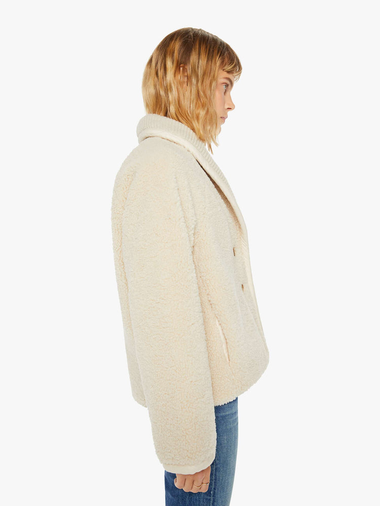 Side view of a woman jacket in a soft faux sherpa in cream with a curved collar, V-neck, slit pockets, buttons down the front, and a slightly boxy fit.