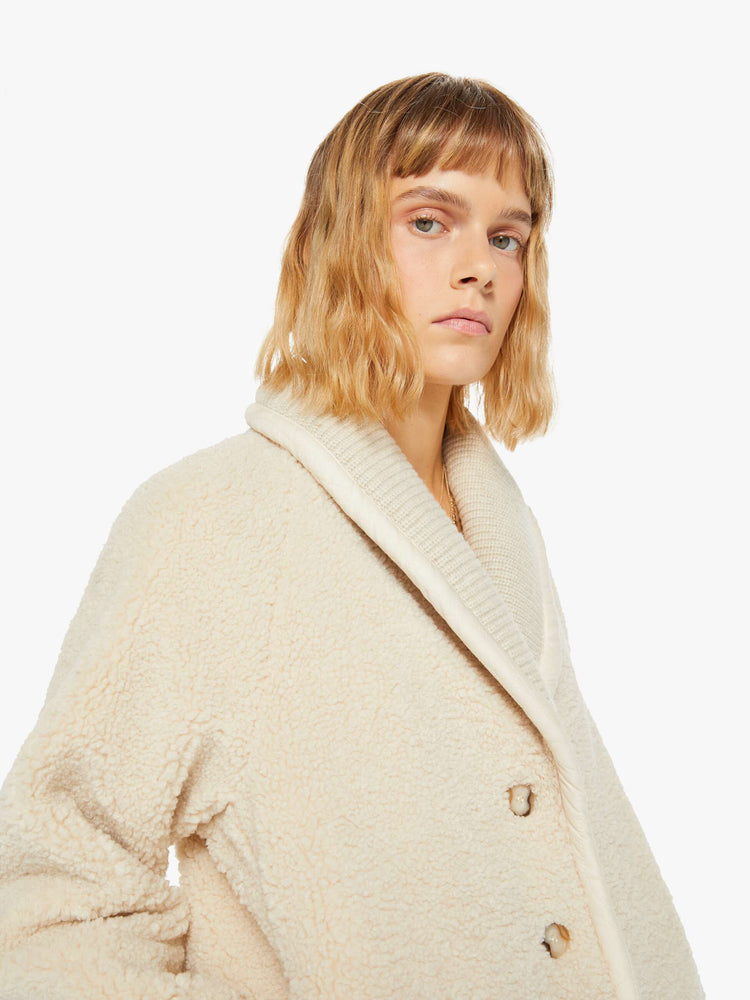 Close up view of a woman jacket in a soft faux sherpa in cream with a curved collar, V-neck, slit pockets, buttons down the front, and a slightly boxy fit.