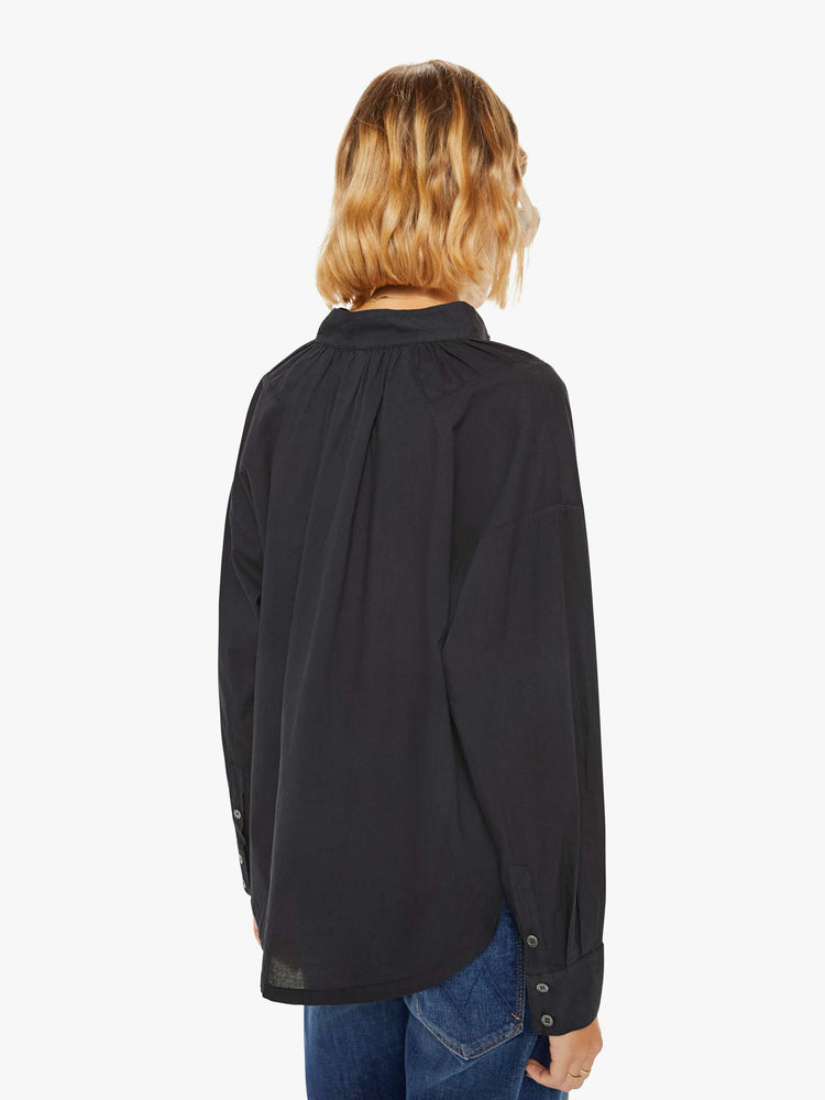 Back view of a woman in a black buttoned V-neck, long balloon sleeves and a curved hem with buttoned details at the hips.