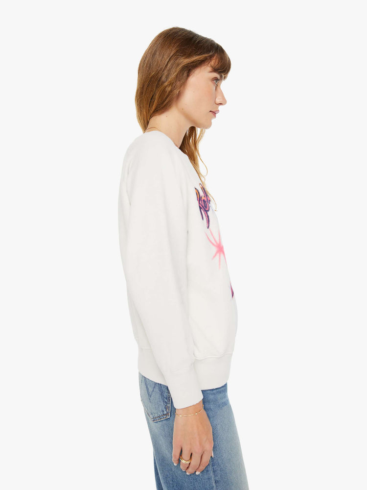 Side view of a woman white crewneck sweatshirt pays homage to the Rolling Stones with the band's iconic tongue-and-lips logo and airbrushed details in hot pink and purple on the front.