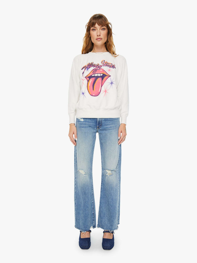 Full body view of a woman white crewneck sweatshirt pays homage to the Rolling Stones with the band's iconic tongue-and-lips logo and airbrushed details in hot pink and purple on the front.