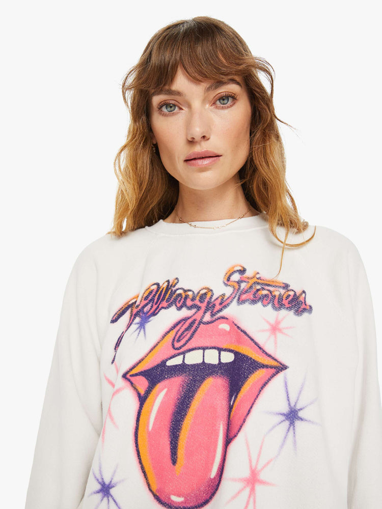 Close up view of a woman white crewneck sweatshirt pays homage to the Rolling Stones with the band's iconic tongue-and-lips logo and airbrushed details in hot pink and purple on the front.
