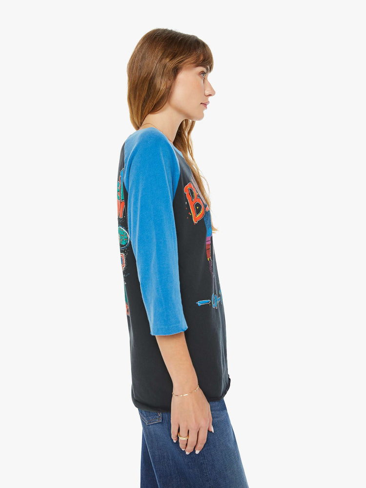 WOMEN  side view of a black with a blue crewneck and sleeves tee that pays homage to Billy Joel's 1978 tour with a colorful graphic portrait on the front and a piano graphic on the back.