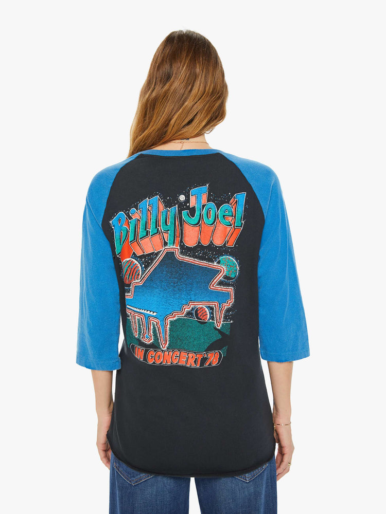 WOMEN back view of a black with a blue crewneck and sleeves tee that pays homage to Billy Joel's 1978 tour with a colorful graphic portrait on the front and a piano graphic on the back.