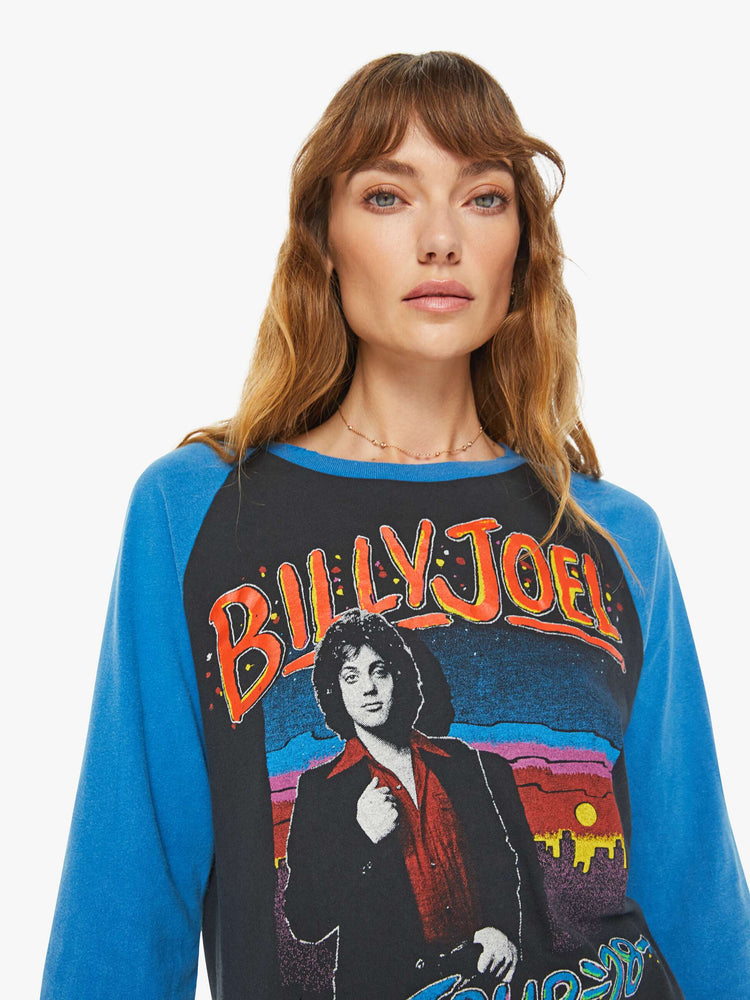 WOMEN close up view of a black with a blue crewneck and sleeves tee that pays homage to Billy Joel's 1978 tour with a colorful graphic portrait on the front and a piano graphic on the back.