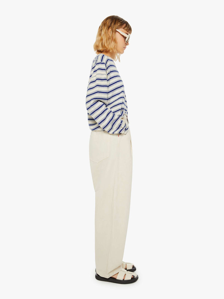 Side view of a woman creamy hue wide leg with a mid rise with pleats at the waist for an even wider fit, an extra-long inseam that puddles at the hem and a colorful woven belt that ties.