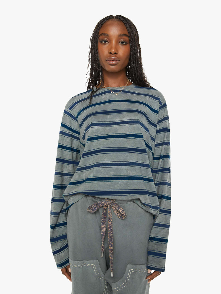 Front view of a woman  long-sleeve crewneck is designed with slightly dropped shoulders and a loose, oversized fit in  a dark grey hue with horizontal stripes in varying shades of blue. 