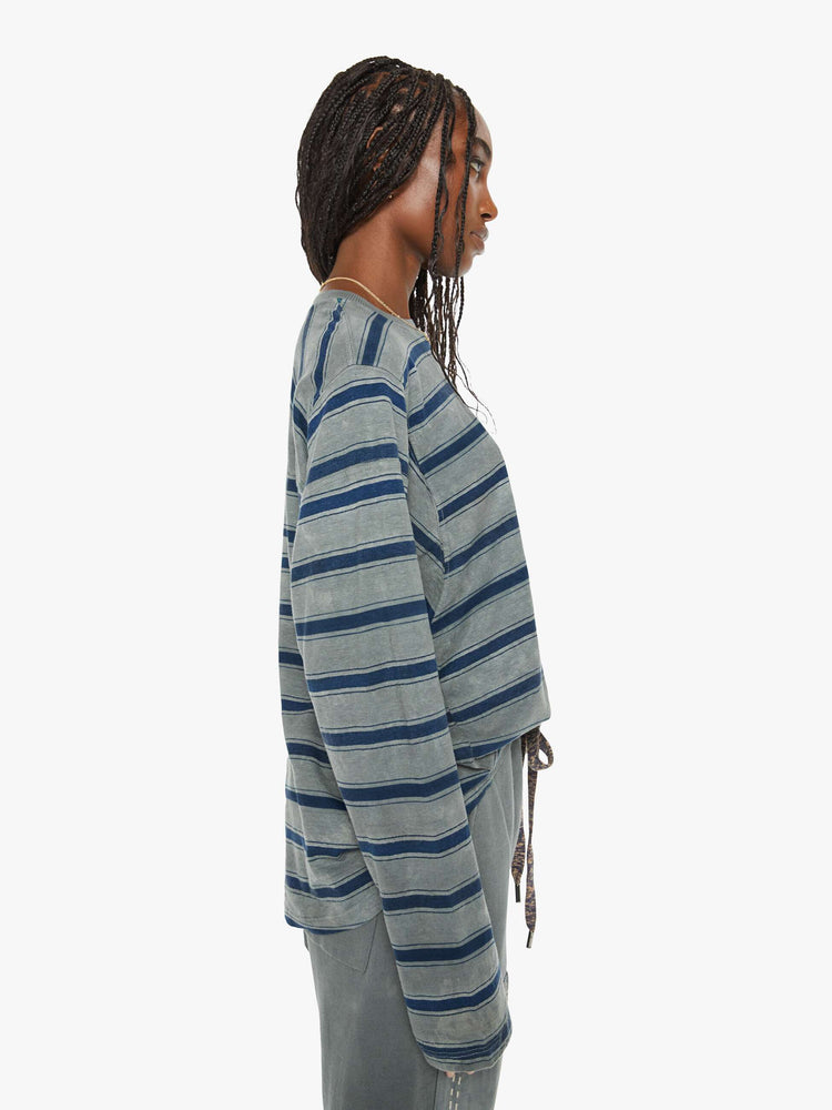 Side view of a woman long-sleeve crewneck is designed with slightly dropped shoulders and a loose, oversized fit in a dark grey hue with horizontal stripes in varying shades of blue.