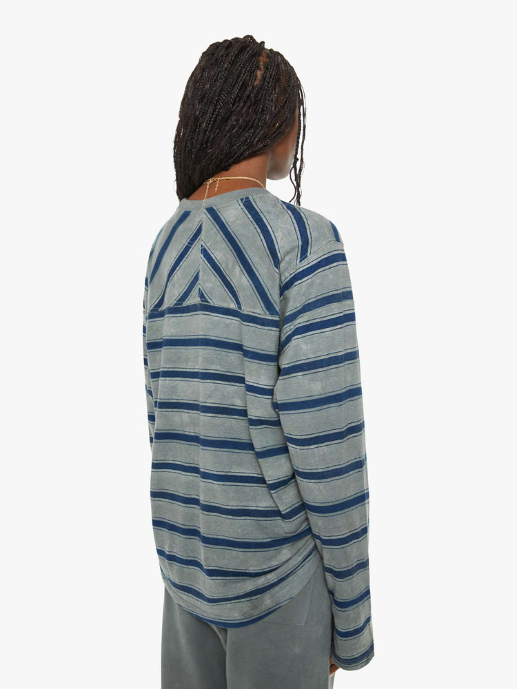 Back view of a woman long-sleeve crewneck is designed with slightly dropped shoulders and a loose, oversized fit in a dark grey hue with horizontal stripes in varying shades of blue.