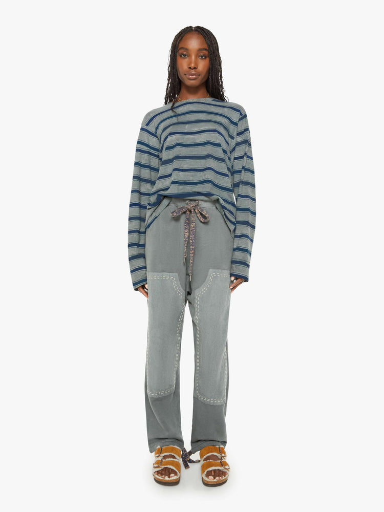 Full body view of a woman long-sleeve crewneck is designed with slightly dropped shoulders and a loose, oversized fit in a dark grey hue with horizontal stripes in varying shades of blue.