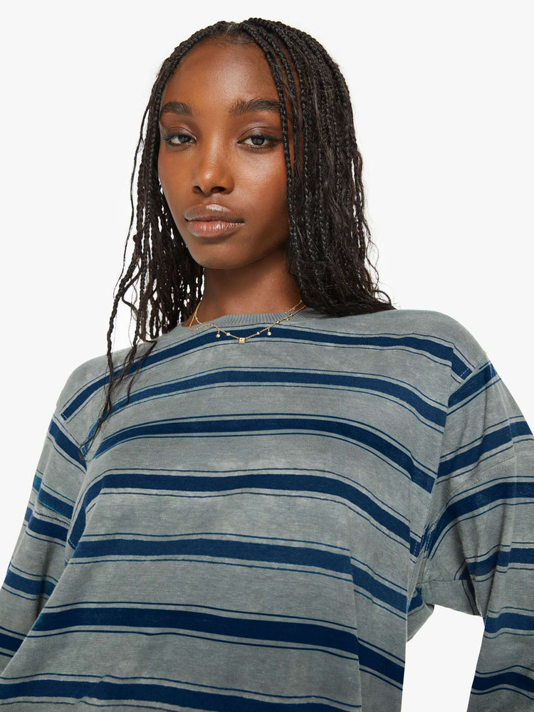 Close up view of a woman long-sleeve crewneck is designed with slightly dropped shoulders and a loose, oversized fit in a dark grey hue with horizontal stripes in varying shades of blue.