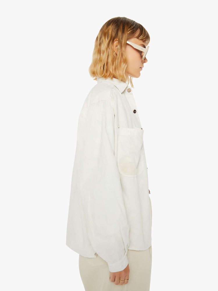 Side view of a woman off white hue shirt with buttons down the front and a boxy, oversized fit with multi colored buttons.