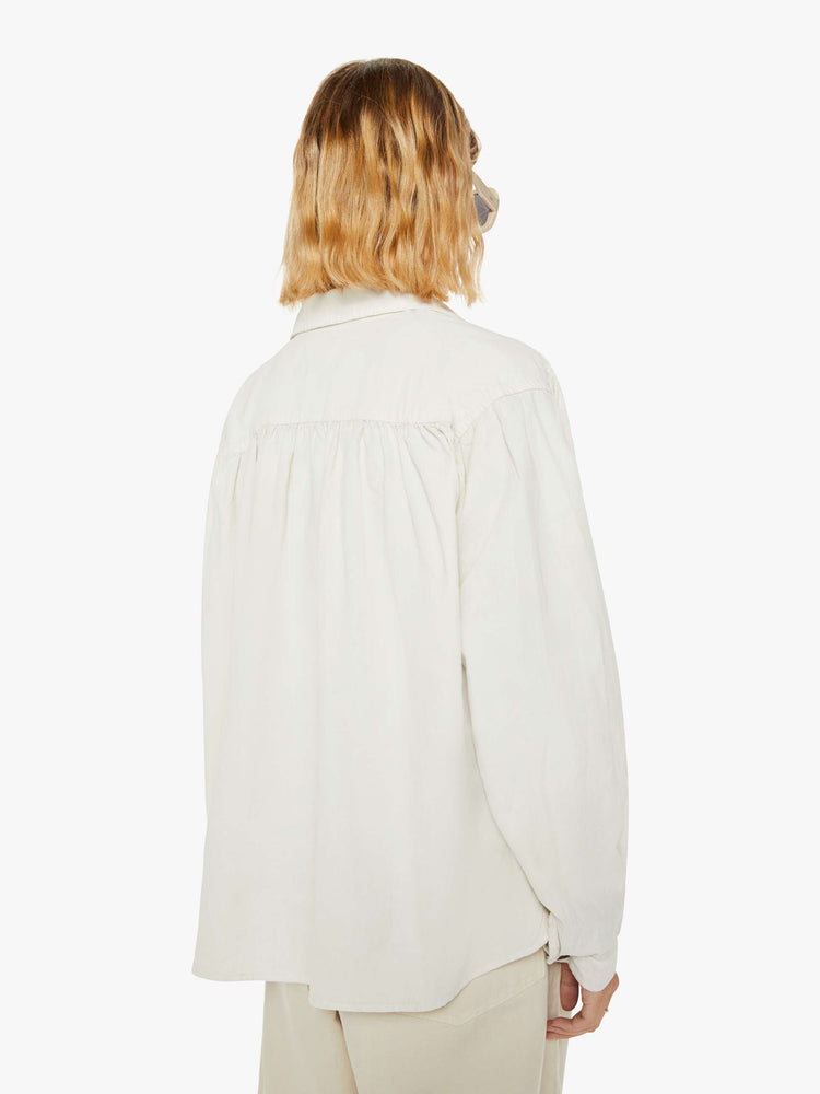 Back view of a woman off white hue shirt with buttons down the front and a boxy, oversized fit with multi colored buttons.